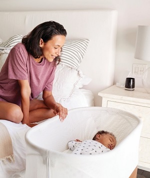 Mother sitting in her bed next to her baby laying in crib, sleeping safely