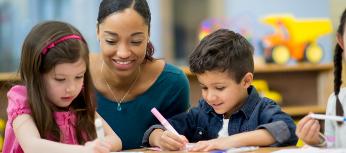 Woman looks on as two children are drawing