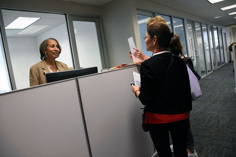 Two woman with paperwork talk to a woman behind a counter
