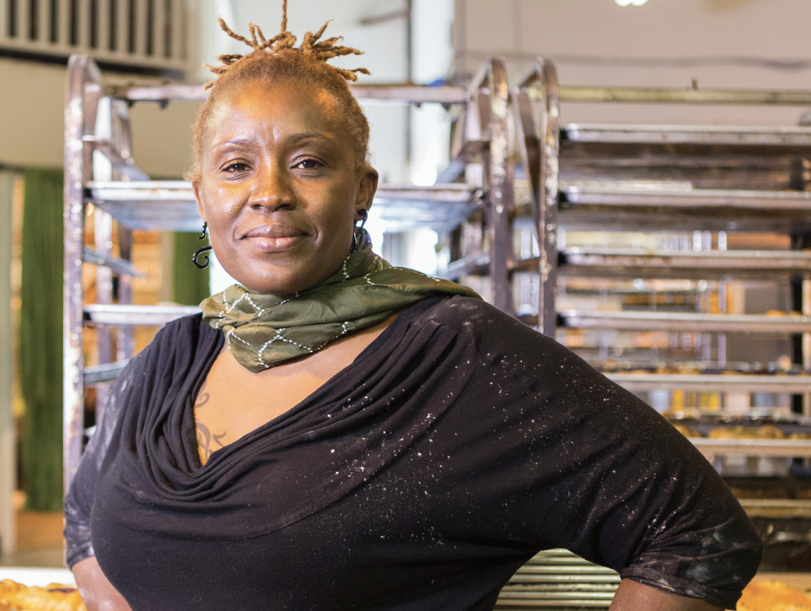 African American woman looking into camera with a half-smile, with racks of food trays behind her.