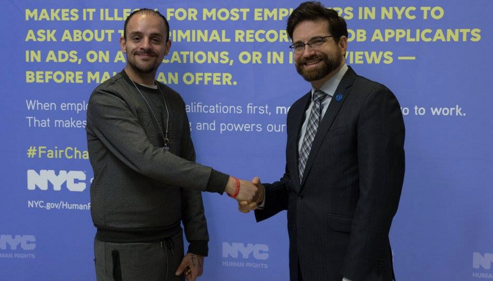 Two men shaking hands and smiling at a camera, with backdrop reading The Fair Chance Act behind them