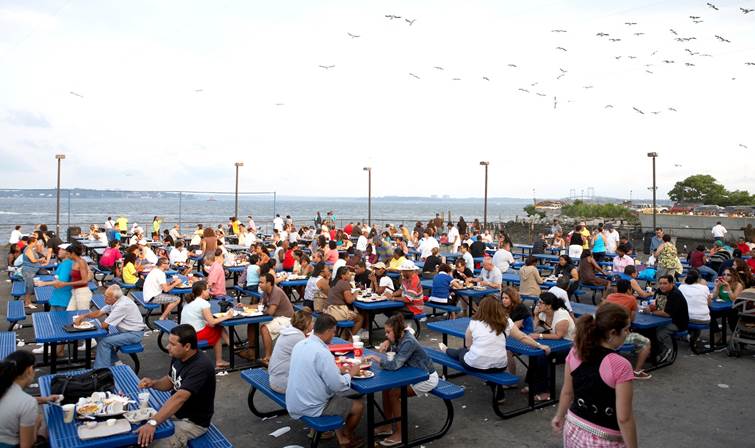A large group of people are sitting at tables outside.  Description generated by AI