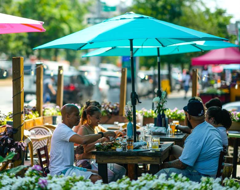 A group of people sitting at a table under a blue umbrella.  Description generated by AI