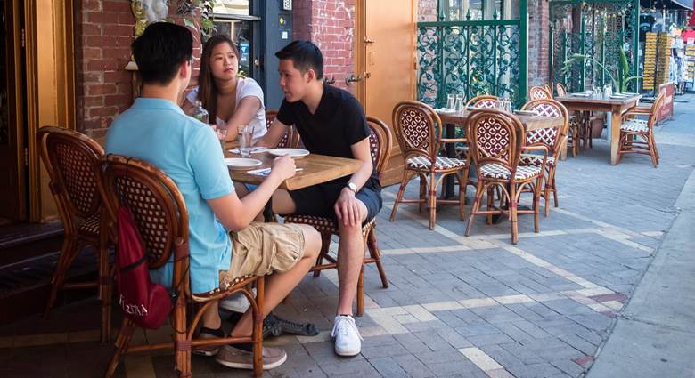 A group of people sitting at a table on a sidewalk.  Description generated by AI