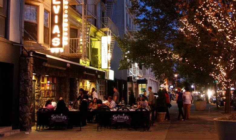 A city street with a restaurant and a tree with lights on it.  Description generated by AI