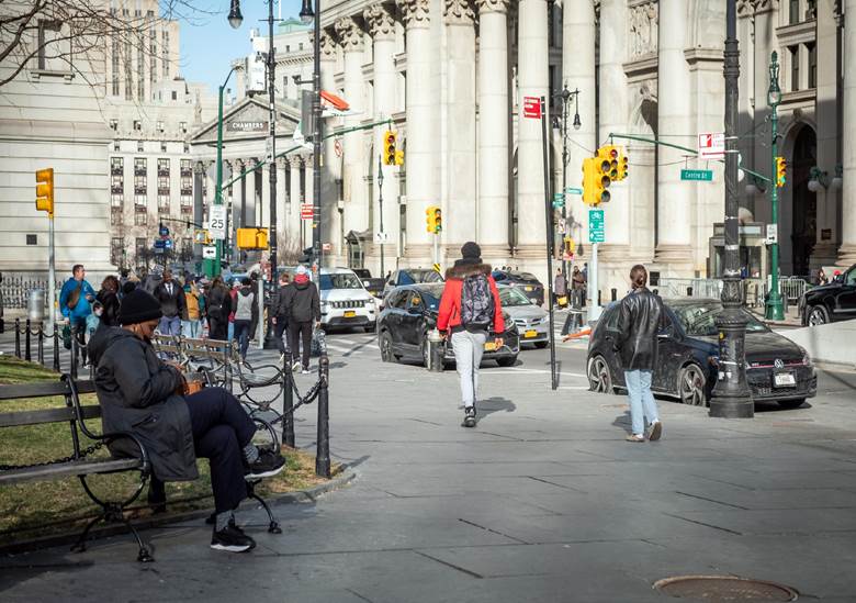 A busy city street with people walking and cars driving.  Description generated by AI