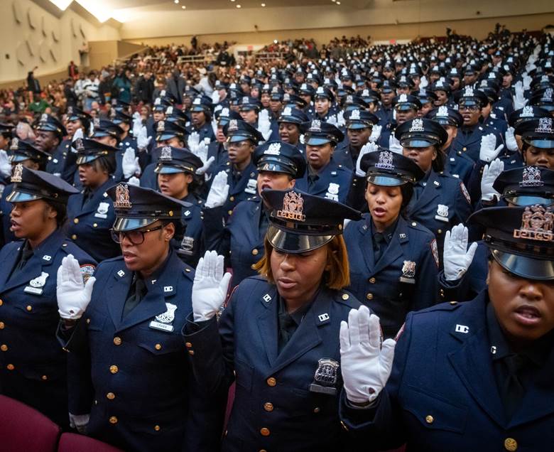 A large group of people standing in a row, all wearing blue uniforms and holding their hands up.  Description generated by AI