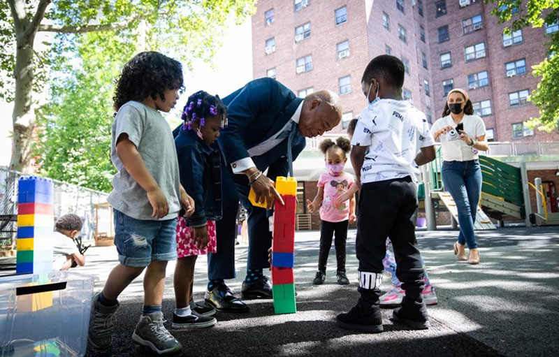 Photo of Mayor Adams playing building blocks with children in a playground.