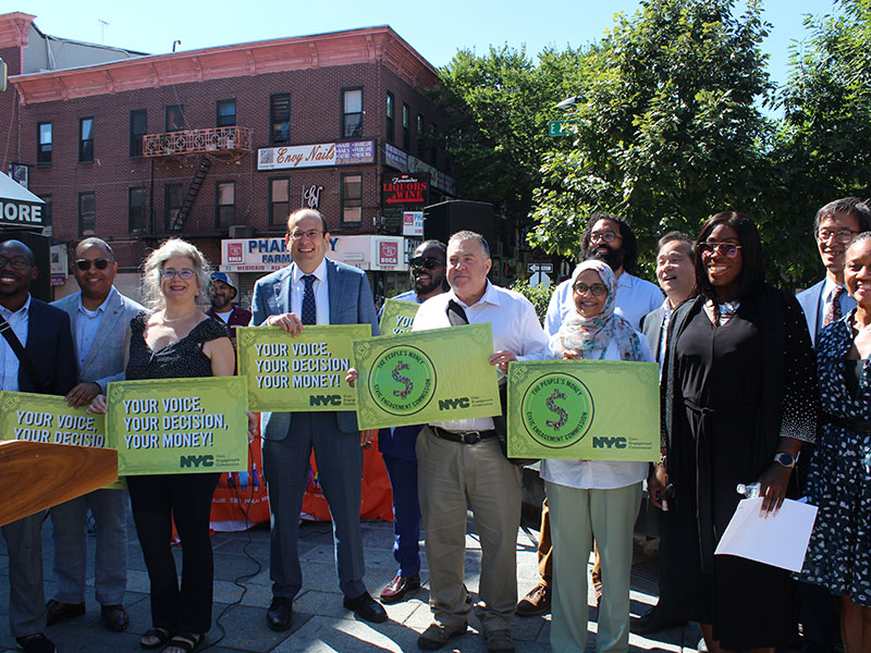Group photo of partners and elected officials holding signs for the People's Money.
