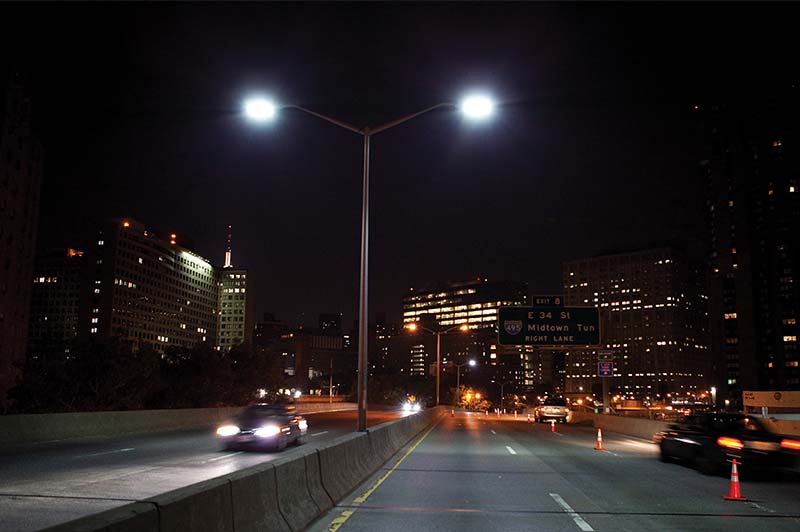 Six lane highway at night illuminated by street lights and the light from cars on the highway. The City is in the background Six lane highway at night illuminated by street lights and the light from cars on the highway. The City is in the background