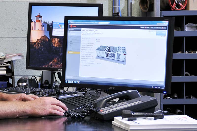 Two hands are visible in from of two computer screens, keyboards, a phone and a flashlight. Shelves with supplies are in the background.  Two hands are visible in from of two computer screens, keyboards, a phone and a flashlight. Shelves with supplies are in the background.