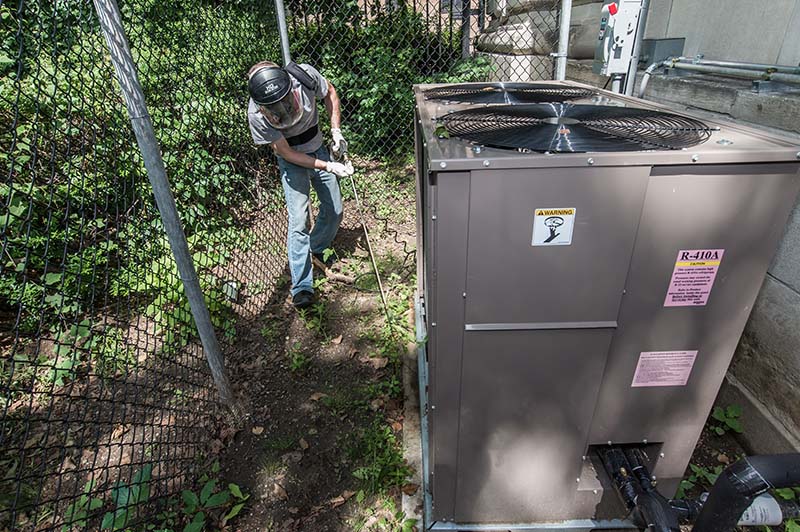 A City staff person wearing a face mask and gloves outside of a facility using a portable coil cleaner to clean condenser coils as part of a preventative maintenance program. A City staff person wearing a face mask and gloves outside of a facility using a portable coil cleaner to clean condenser coils as part of a preventative maintenance program.