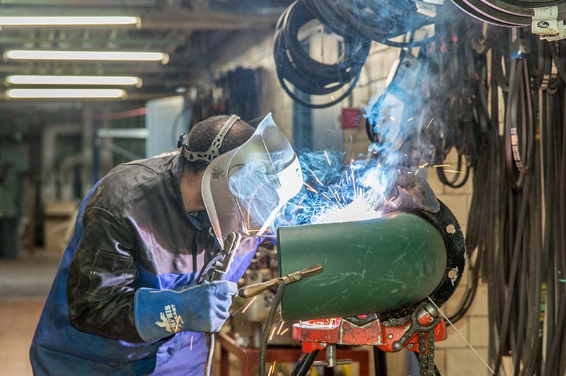A pipe fitter in a workshop welding pipes together for a chilled water pump replacement project.