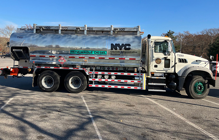N Y C D C A S blue electric van near a brick wall and an charging station.
                                           