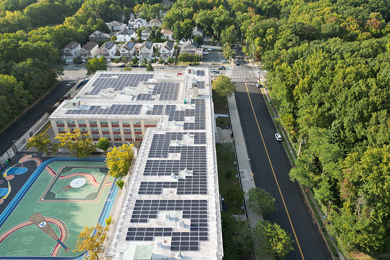 An arial view of a New York City school with newly installed solar panels, with trees surrounding the building.