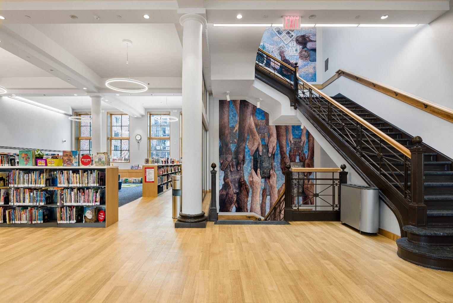 A mural of hands of varying skin tones holding books fills a stairwell.