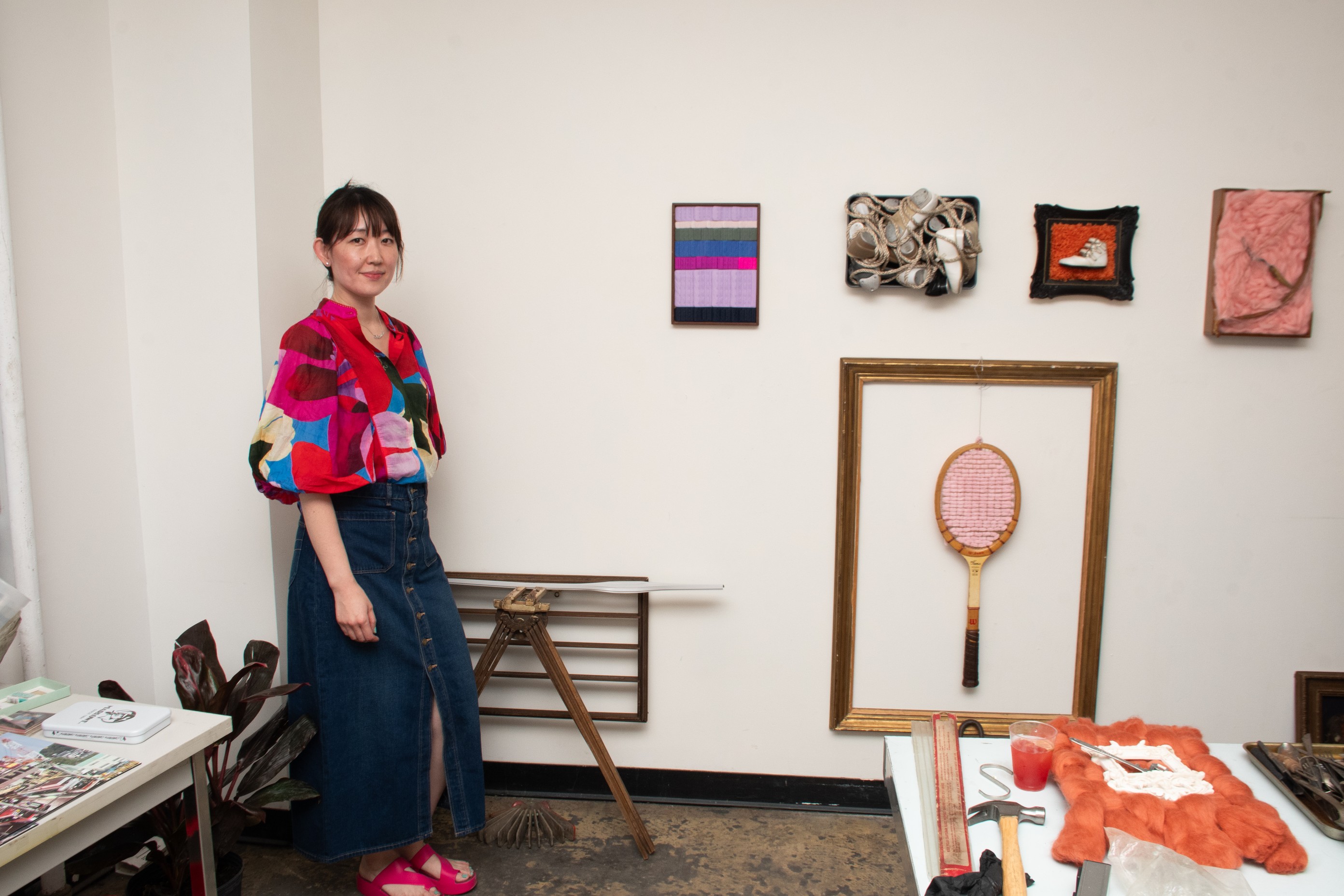 Natsuki stands beside her work with shoes, bra clasps, and a tennis racket.
