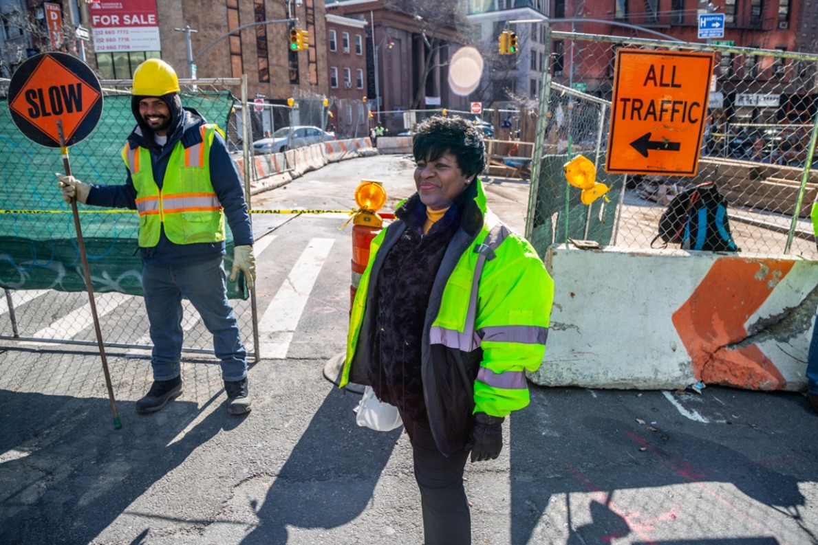 A community construction liaison stands next to a project site