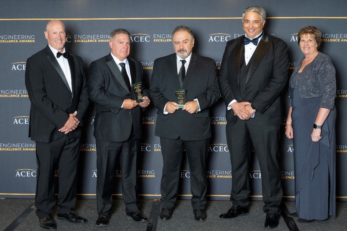 group photo of five people at awards event holding two awards