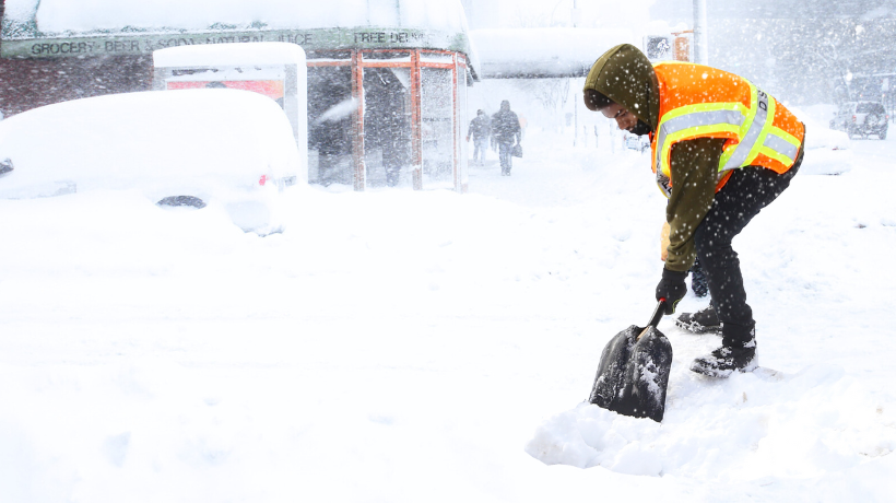 Person in a high visibility vest shoveling a snow-covered sidewalk
                                           