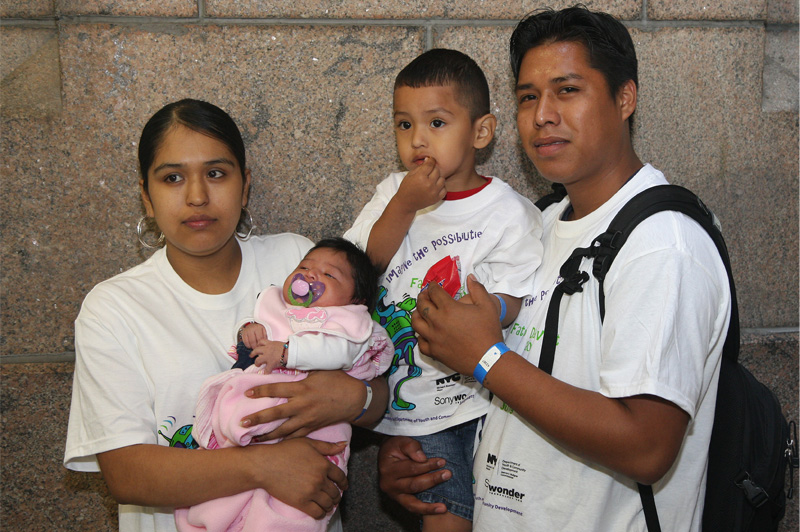 man, woman, boy child and baby standing against a wall and posing for image