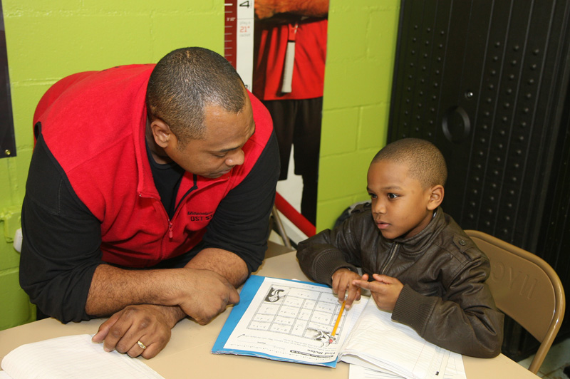 man and boy sit at desk in classroom working on worksheet