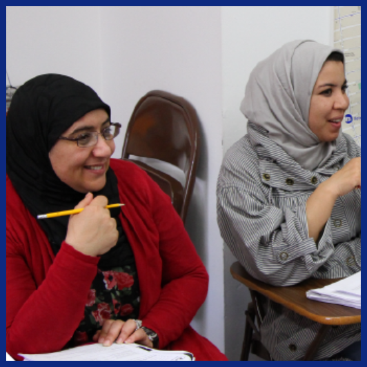 two women smiling while sitting at desks in a classroom