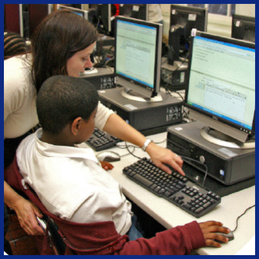 teacher showing student how to use keyboard at computer desk