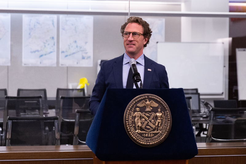 Commissioner Iscol (center) standing behind a podium.
