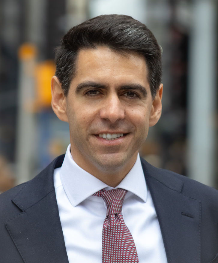 Lucy Joffe, Deputy Commissioner for Policy and Strategy Patrick Love, Deputy Commissioner for the Office of Development, in a suit and tie smiling against a blurred urban background