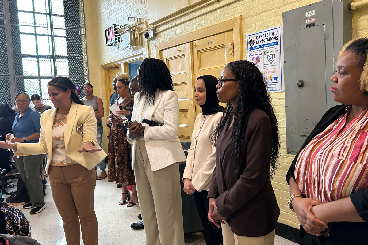 A photo of a group of people standing in a school cafeteria, greeting students and staff.