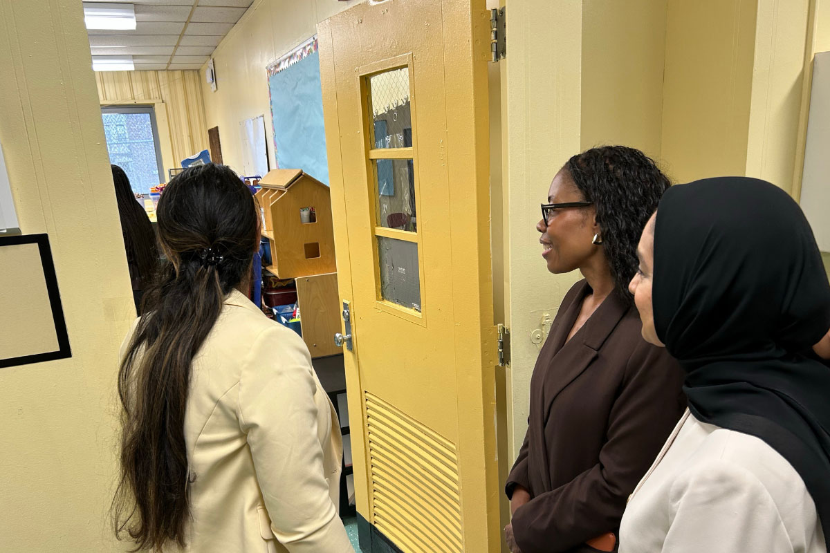 A photo of a group of people visiting a school. The group is looking inside a classroom.