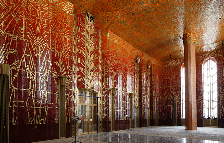 Red room with high ceilings and pillars, walls and ceiling covered with red mosaic tile with gold designs