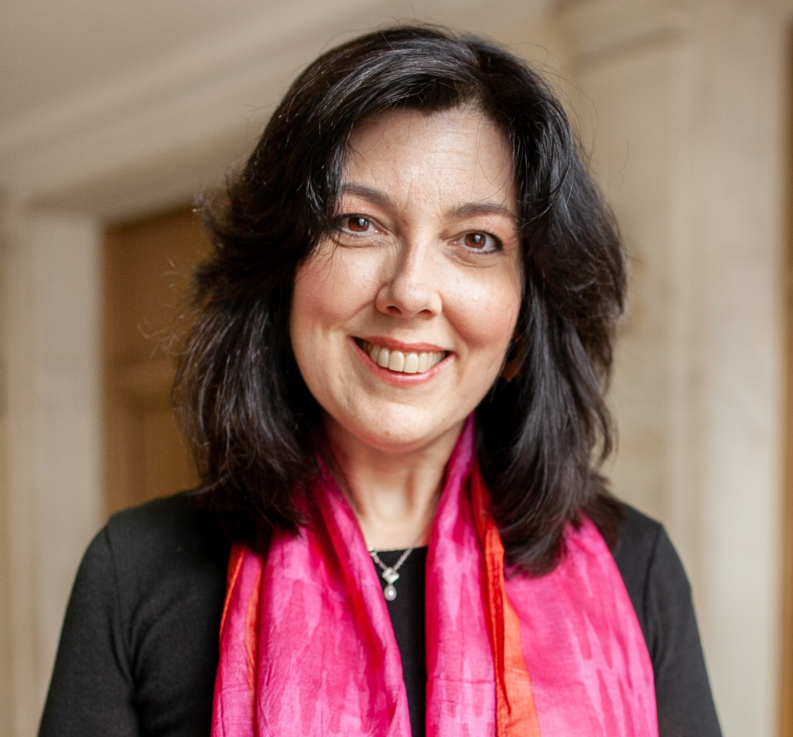 Photo of smiling person wearing a pink scarf; blurred aerial photo of New York City skyline in the background