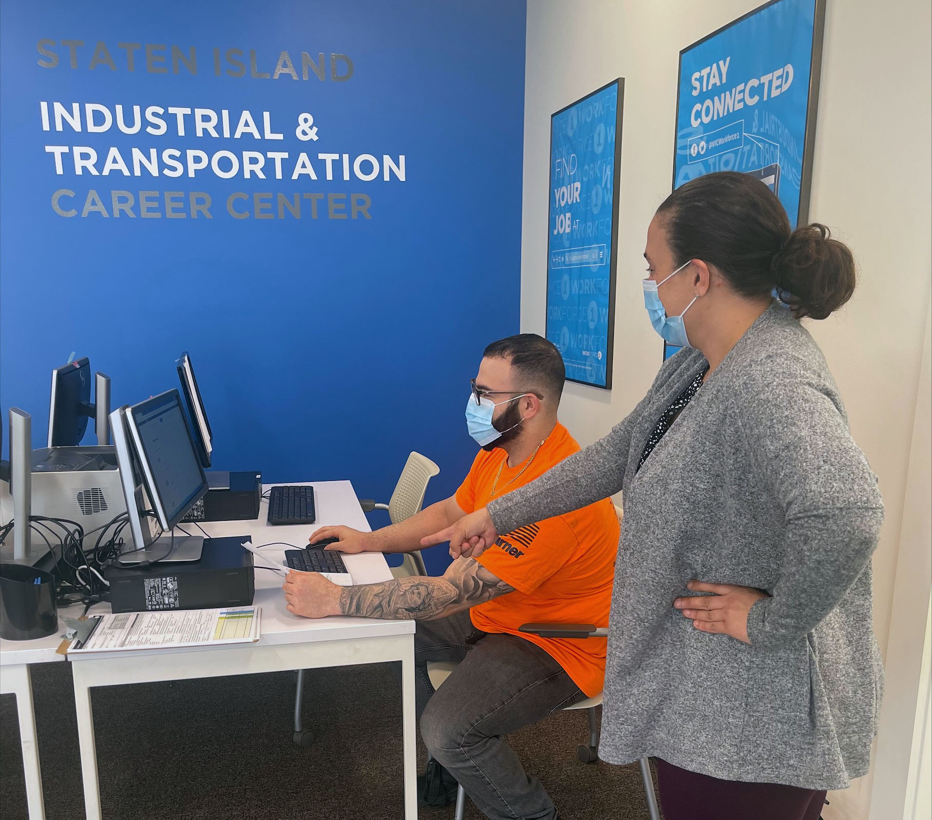 man seated at computer in Workforce1 Career Center with woman standing and giving him direction