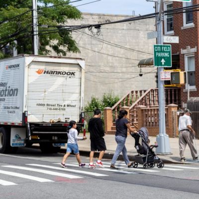 A white box truck parked at the curb and pedestrians walk on a crosswalk.