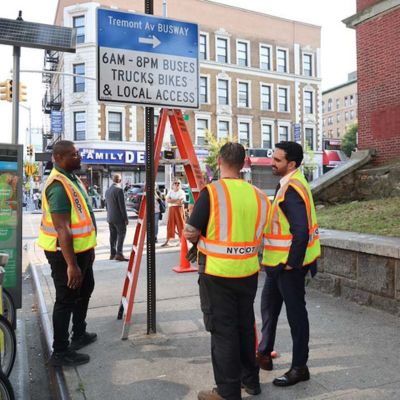 Mayor Mamdani and two D O T employees stand next to a newly installed Tremont Avenue Busway sign in the Bronx.