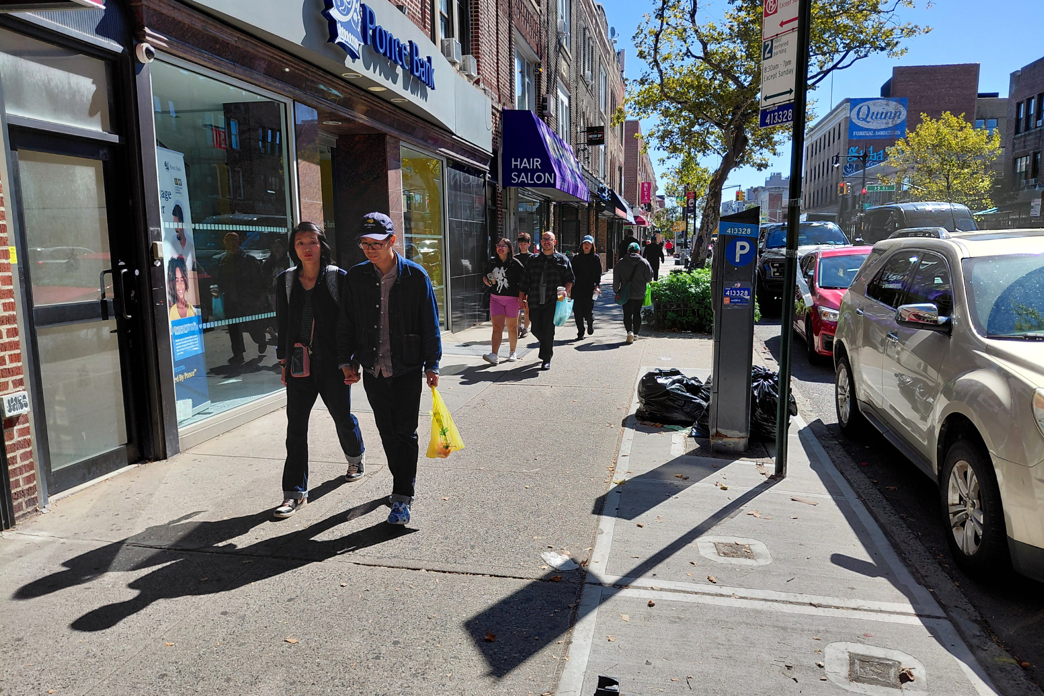 People stroll along a wide sidewalk in a busy neighborhood in New York City.