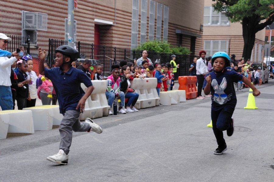 Two young students wearing bicycle helmets run along a street closed to vehicular traffic in front of a school 