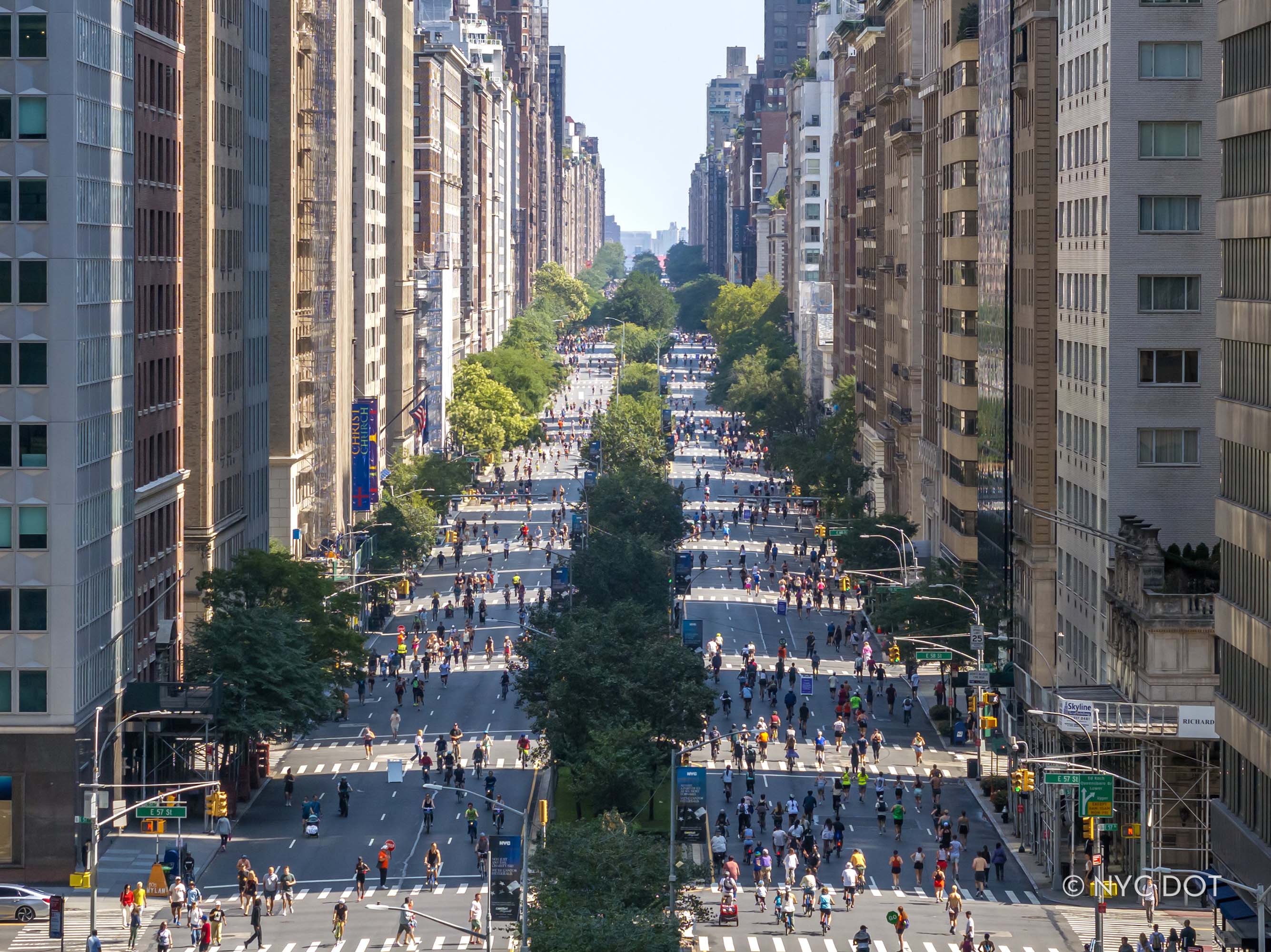 An aerial view of Park Avenue with people walking, running, and bicycling on both sides of the tree-lined avenue.